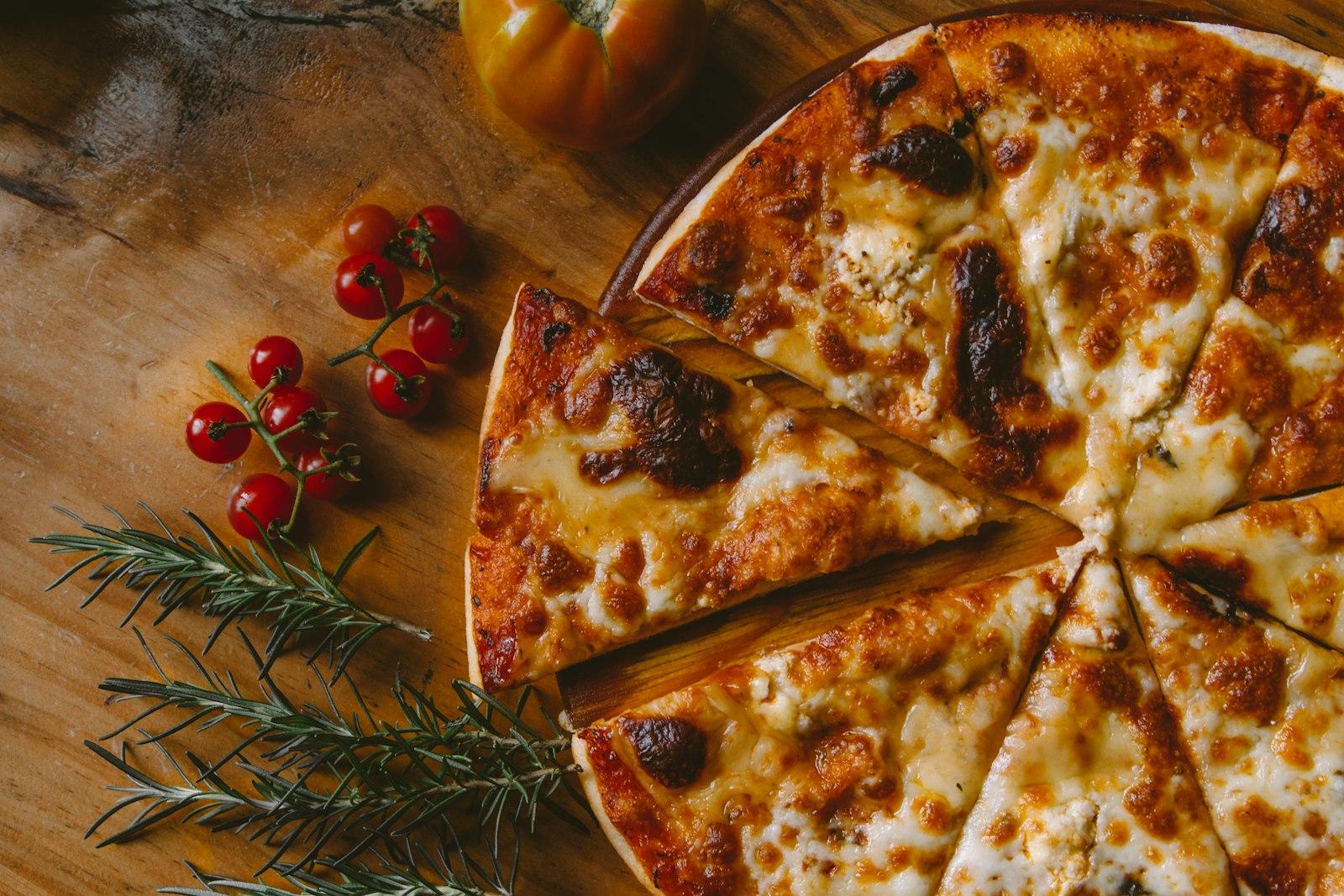 A freshly baked pizza on a wooden board with rosemary and cherry tomatoes